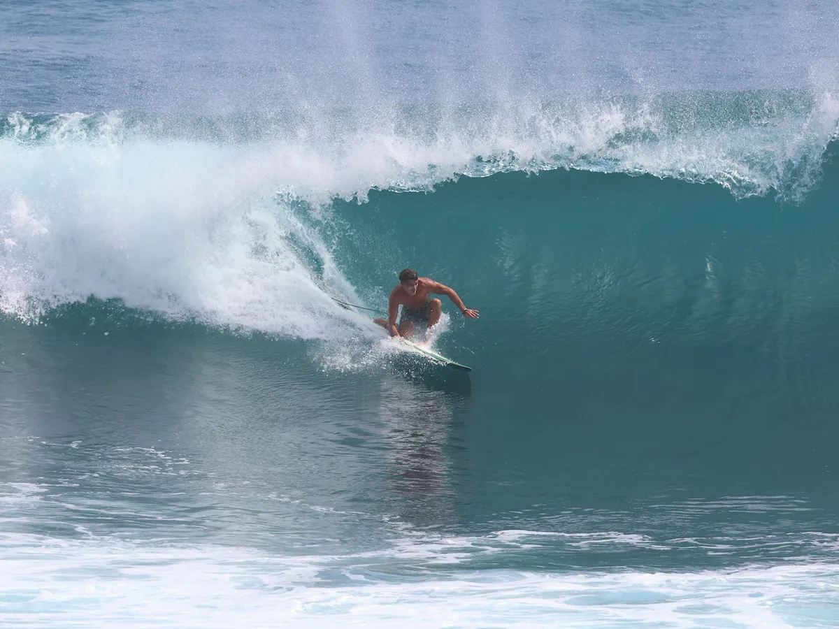 Experienced surfer performing a sharp bottom turn beneath a powerful breaking wave