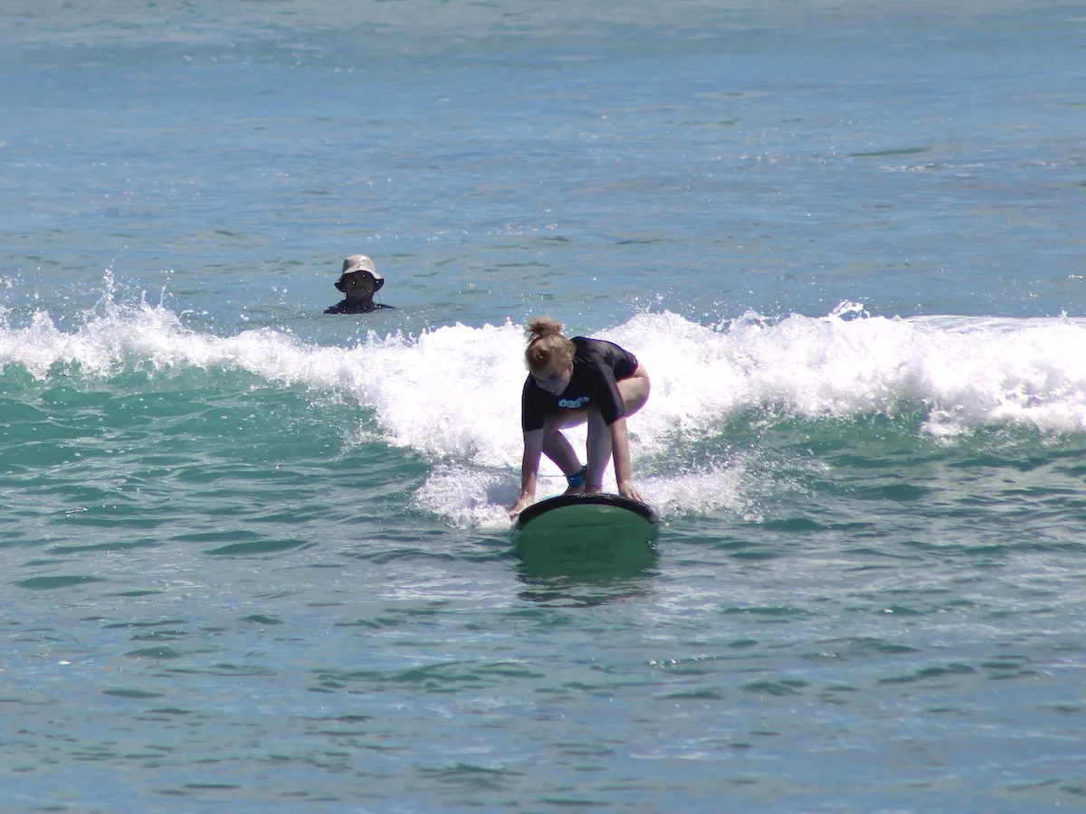 Beginner surfer learning to stand up on a surfboard while riding a small breaking wave